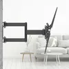 A black TV wall mount is attached to a white wall, with a sofa and tables in the background. Podgląd zdjęcia produktu