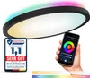 A hand holding a smartphone displaying a smart light app, with a ceiling light in the background emitting colorful light. A quality seal is also visible. Produktbild-Vorschau