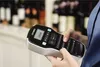 A person is holding and using a DYMO LabelManager 160 in what appears to be a retail environment with shelves of bottles in the background. Produktbild-Vorschau