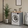 A washing machine cabinet with a wooden top, placed in a bathroom setting with a plant and towels. Náhľad obrázku produktu