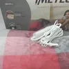 A close-up of a heated blanket with its power cord and controller, placed on a patterned surface. The background shows a partial view of packaging with product information and a person in the background. Anteprima dell’immagine prodotto