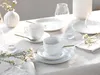 A table setting with white porcelain cups and saucers, gold accents, and floral decorations. Produktbild-Vorschau