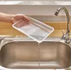 A hand holding a clear plastic tray over a stainless steel sink, with water dripping from the tray into the sink. A faucet is visible in the background. Voir les images du produit