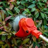 A close-up view of an orange electric hedge trimmer with a circular blade, cutting through green and red leaves of a bush. Produktbild-Vorschau