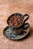 Two coffee cups stacked on a saucer, filled with coffee beans, on a textured surface. Podgląd zdjęcia produktu