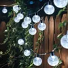 String lights are draped along a wooden fence and green foliage. Produktbild-Vorschau