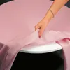 A hand is shown adjusting a pink tablecloth on a round table. Produktbild-Vorschau