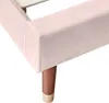 A close-up view of the corner of a pink upholstered bed frame with wooden legs. Náhľad obrázku produktu