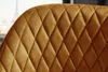 A close-up view of a quilted mustard yellow fabric, likely a chair or stool, with a blurred background showing a cityscape and the Eiffel Tower. Produktbild-Vorschau