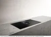 A black induction cooktop with a built-in ventilation system is shown on a concrete countertop against a white wall. Náhled obrázku produktu