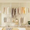 A white telescoping garment rack with multiple shelves and hanging clothes, set up in a room with a bed in the foreground. Produktbild-Vorschau
