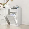 A white bathroom cabinet with a flip-down laundry hamper and a drawer, placed on a light-colored floor next to a sink. Anteprima dell’immagine prodotto