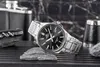 A watch is displayed on rocks with a flask and a corkscrew in the background. Voir les images du produit