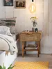 A bedside table next to a bed, with a lamp and some decorative items. Produktbild-Vorschau