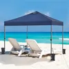 A navy blue pop-up canopy tent is set up on a sandy beach with two white lounge chairs underneath it. The ocean and blue sky are in the background. Produktbild-Vorschau