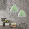 Two green pendant lamps hang above a table with a pitcher, apples, books, and a chair in the background. Náhled obrázku produktu