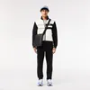 A man wearing a Lacoste outfit and a cap, standing against a white background. Produktbild-Vorschau