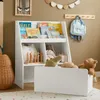 A child's room with a white bookshelf filled with books and toys, a light blue backpack hanging on a wall hook, and a woven basket. A rug with colorful dots is on the floor. Náhľad obrázku produktu
