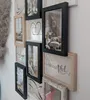 A wall decorated with a collage of picture frames of various sizes and orientations, some containing photos and others with decorative text or drawings. Produktbild-Vorschau