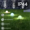 Outdoor garden scene with illuminated sphere lights on the grass, with a stone wall and rain in the background. Produktbild-Vorschau