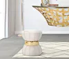 A cream and gold ottoman is placed on a rug in front of a console table with a glass top and a gold butterfly-shaped base. Anteprima dell’immagine prodotto