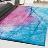 A rug with an abstract pattern is shown in a living room setting, partially under a sofa. Náhled obrázku produktu