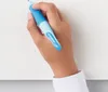 A hand holding a blue ergonomic pencil over a white surface. Produktbild-Vorschau