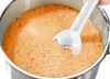 An immersion blender being used to blend an orange liquid in a pot. Produktbild-Vorschau