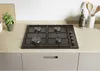 A black gas hob is installed on a light wood countertop, with kitchen cabinets below. There are some kitchen accessories and a plant on the countertop. Anteprima dell’immagine prodotto