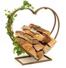 A heart-shaped log holder decorated with artificial ivy, filled with firewood, on a white background. Produktbild-Vorschau