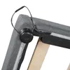A close-up view of the corner of a gray upholstered bed frame, showing a black circular component with wires attached. Produktbild-Vorschau
