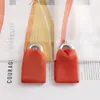 Close-up of two orange fabric tie-backs with silver grommets attached to sheer curtains with a printed pattern. Produktbild-Vorschau