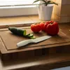 A cutting board with a cucumber, tomatoes, and a knife on a kitchen counter. Produktbild-Vorschau