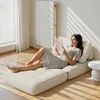 A woman is relaxing and reading a book on a modular sofa/daybed in a well-lit room with sunlight streaming through blinds. Produktbild-Vorschau