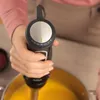 A person is holding a black immersion blender over a pot of yellow soup. Produktbild-Vorschau