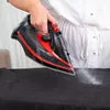 A person is ironing a dark fabric with a black and red steam iron. Náhľad obrázku produktu