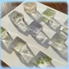 Several clear cubes containing dried flowers and leaves are arranged on a white surface, casting shadows. Voir les images du produit