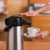 A hand is pressing a button on a coffee airpot to dispense coffee into a cup. Produktbild-Vorschau
