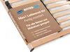 A close-up view of a wooden slatted bed base with a product information label wrapped around it. Produktbild-Vorschau
