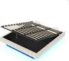 A bed frame with the mattress support mechanism lifted, revealing storage space underneath. The bed frame is upholstered in beige fabric and has blue LED lighting around the base. Voir les images du produit
