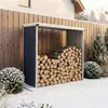 A metal firewood storage shed filled with logs, set against a wooden fence in a snowy outdoor environment.