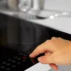 A hand is shown pressing a button on a black glass ceramic stovetop. Produktbild-Vorschau