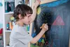 A young boy is drawing on a chalkboard with chalk. Voir les images du produit