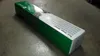 A long, rectangular box with green and white branding sits on a concrete floor. Voir les images du produit