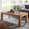 A wooden coffee table in a living room setting, with a sofa and window in the background. Produktbild-Vorschau