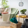A cozy living room setup with blankets draped over a chair and stacked on a table. Náhled obrázku produktu