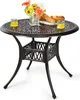 A round patio table with a decorative top and a basket-like base, set against a white background. It is adorned with a vase of flowers, two glasses of yellow liquid, and a plate of bread.