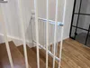 A white metal baby gate is installed on a wooden staircase. Voir les images du produit