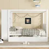 A white wooden canopy bed with storage and a side cabinet, set up in a child's bedroom. Produktbild-Vorschau