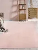 A pink rug is laid out in a room with a sofa and a wooden shelf unit. Produktbild-Vorschau